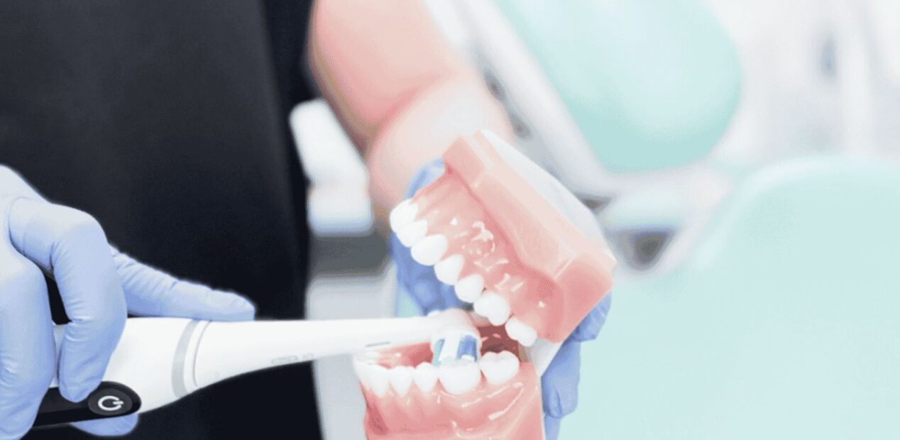 Une personne portant des gants utilise une brosse à dents électrique pour nettoyer un modèle dentaire de dents dans un cabinet dentaire chez iDental Studio.