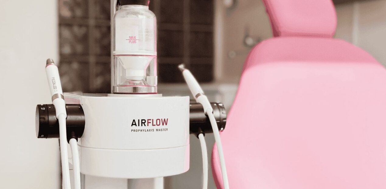 Close-up of dental equipment labeled AIRFLOW Prophylaxis Master next to a modern pink dental chair in the clean, bright iDental Studio dental practice in Geneva.